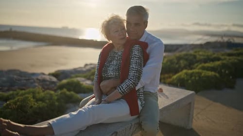 Senior Couple Embracing on Bench at Sunset By the Sea