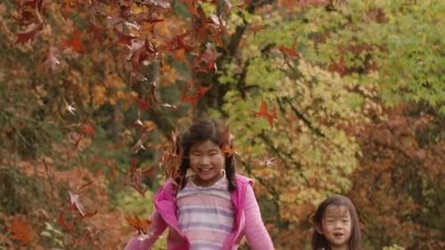 Two Girls Throwing Colorful Autumn Leaves in Forest