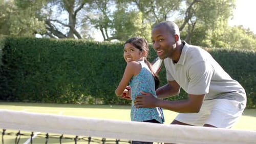 Playing tennis, father teaching daughter how to hit ball on court