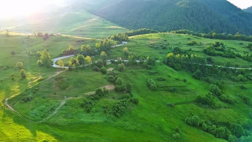 A Road Passes Hills Covered with Spruce Forests and Meadows Against a Cloudy Sky