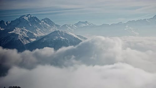 Time lapse shot of flying clouds between snowy mountain peaks during sunny day