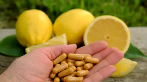 Hand Holding Capsules with Fresh Lemons Close Up