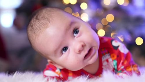 Adorable baby face with cute plump cheeks looks up. Sweet kid lies on a fluffy plaid close up.