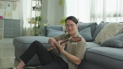 Young Adult Plays Guitar Sitting on Floor