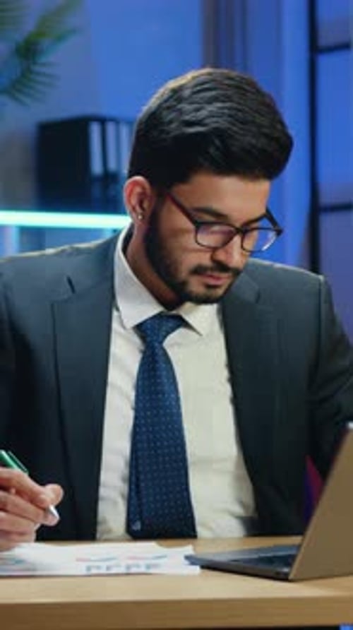 Man in Formal Wear Typing on Computer and Writing Out Important Notes Into Report on Night Lighted
