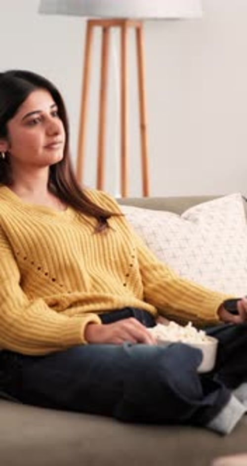 Watching tv, popcorn and remote with woman on sofa for relax, channel surfing and streaming service