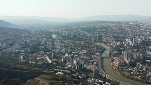 Aerial view of Tbilisi, Georgia and Kura river running through the city. Mountainous background. Est