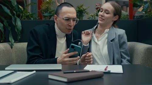 Office Couple Listening to Music in Wired Headphones while Doing Paperwork