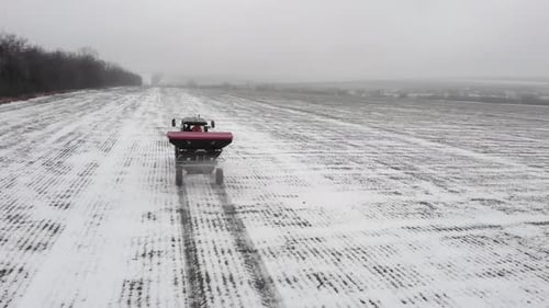 Tracteur épandant des engrais et des pesticides en hiver sur un champ de neige