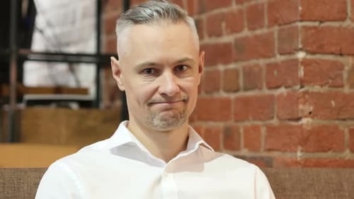 Man Smiles into Camera in Brick Walled Office