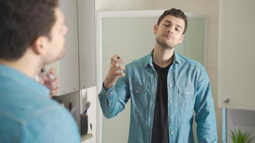 Young Man Sprays Cologne in Bathroom Mirror