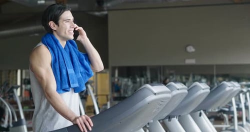 Portrait of a guy in a gym while resting between a workout and the other uses his phone to watch s