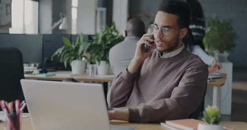 Office Employee African American Man Discussing Work on Mobile Phone and Using Laptop