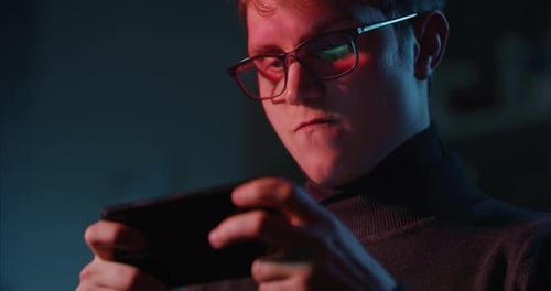Cinematic shot of an young man gamer is using a smartphone for playing latest innovated technology
