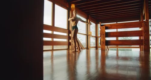 Dancer performs a graceful pose under natural light in a wooden studio space