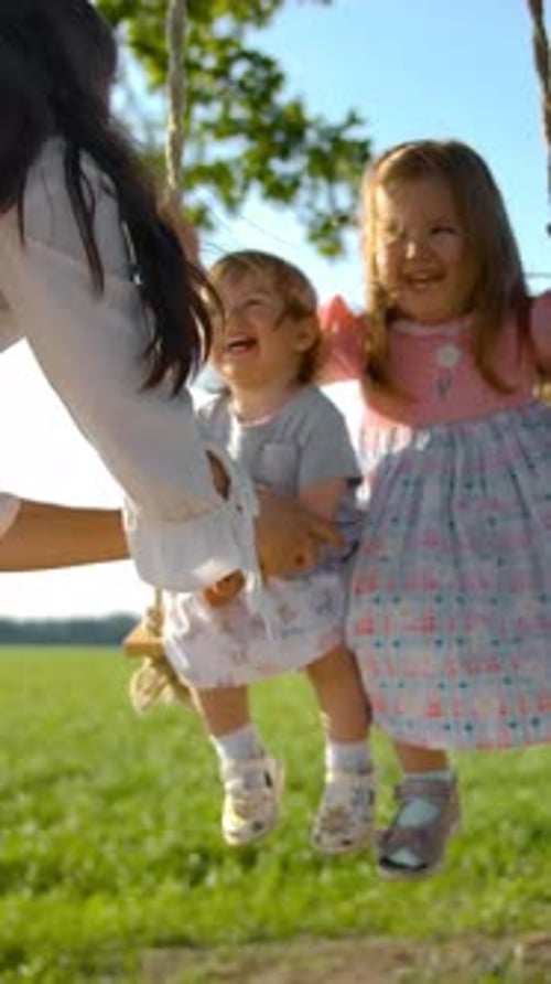 Girls Laughing on a Swing in a Grassy Field