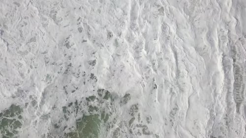 Stormy sea with waves breaking, white foam and beach sand dragged into the sea