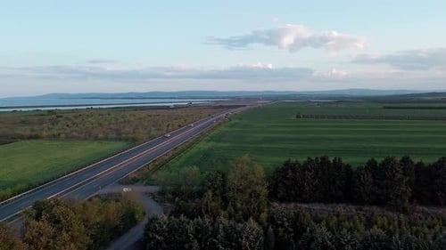 Road with Cars and Trucks on It Passes Through Fields Under a Colored Sky