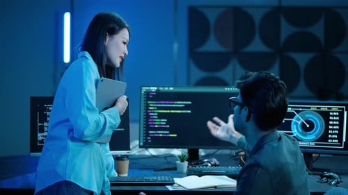 Asian woman and man discussing programming code and data analytics on computer screens
