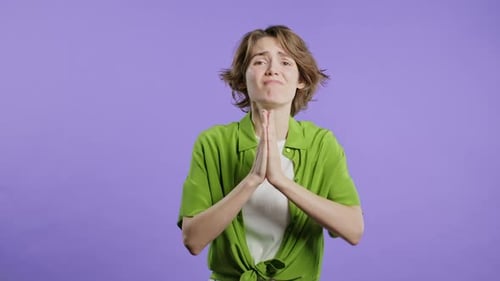 Young Woman Pleading, Apologetic Against Purple Background