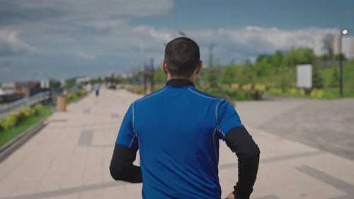 View From the Back A Man in Sportswear Runs Through a Landscaped City Park Public Urban Spaces for