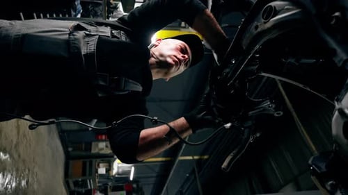 Vertical Video Low Shot an Auto Mechanic at a Service Station is Trying to Remove the Base on Which