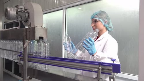 Technologue dans une usine d'embouteillage vérifiant les bouteilles d'eau avant expédition.