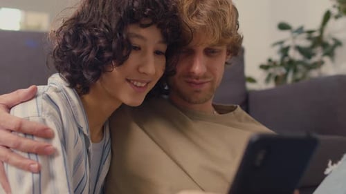 Smiling Couple Embracing and Looking at Phone Indoors