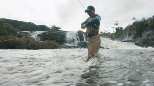 Man Fly Fishing in River Near Waterfall