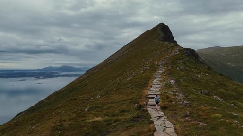 Young woman hiking uphill on scenic stone mountain path with trekking poles in Norway, aerial drone