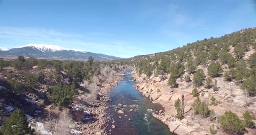 Drone view of a green river in Colorado rocky ground with snowy mountains in the background
