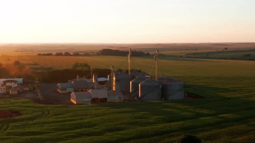 Grain silo factory warehouse facility with tanks and afternoon sunset over valley in industrial coun