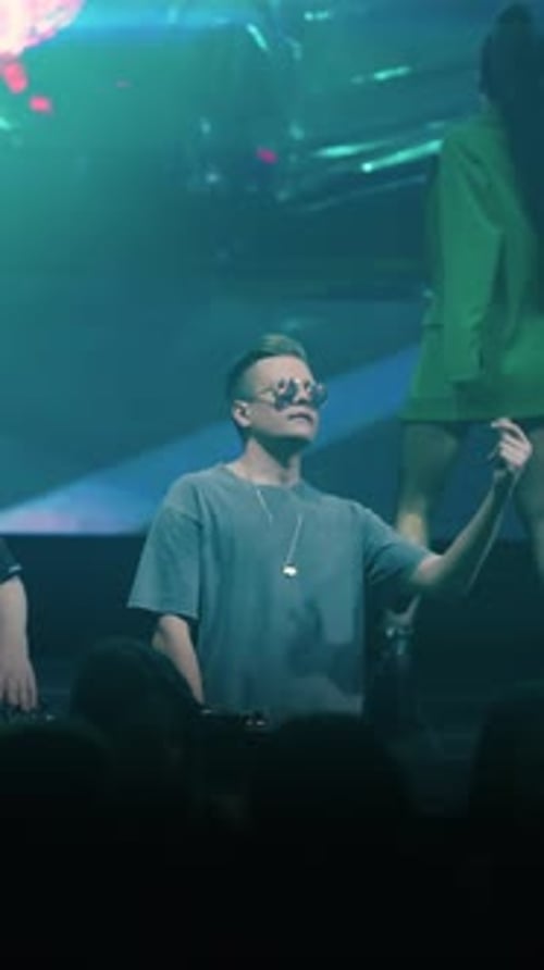 DJ Performing on Nightclub Stage with Colorful Neon Lights and Stylish Dancer in Green Blazer