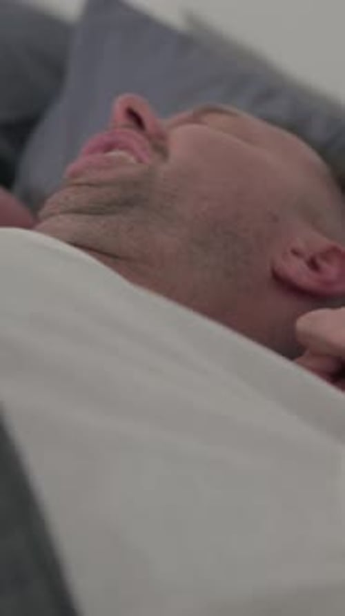 Gros plan d'un homme décontracté se réveillant du sommeil dans son lit, vidéo verticale