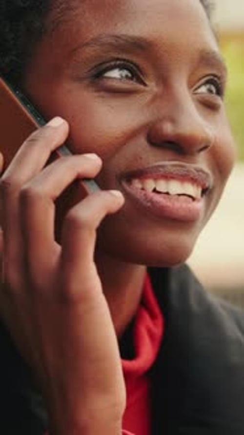 Vertical video, Smiling young woman talking on mobile phone sitting outside on city street