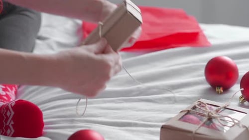 Hands Wrapping Christmas Presents on Bed at Home