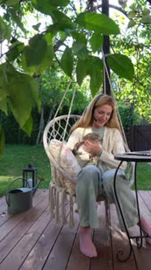Woman Holding Cat Sits Outside on Hanging Chair