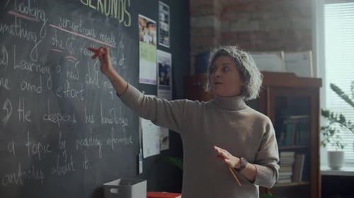 Woman Teacher Explains Lesson at Blackboard