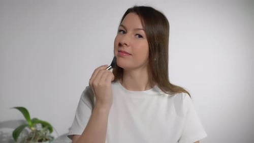 Woman Applies Makeup with Brush in Home Setting