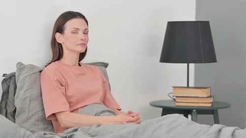 Femme avec les pouces levés regardant la caméra alors qu'elle est assise dans son lit