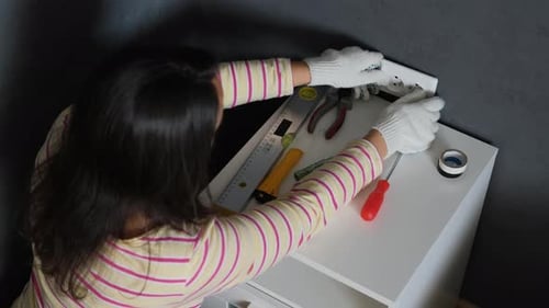 Female Repairs Electrical Outlet in Bedroom