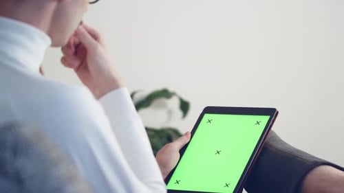 Handheld shot of young man using tablet with green screen chromakey.