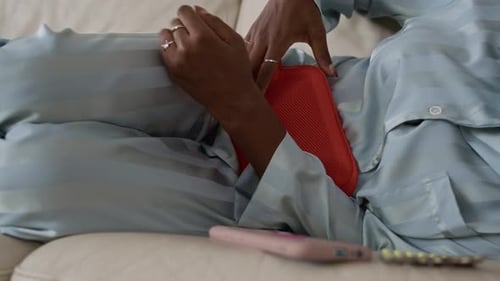 Fatigued Woman Lying on Sofa with Heating Pad during Period