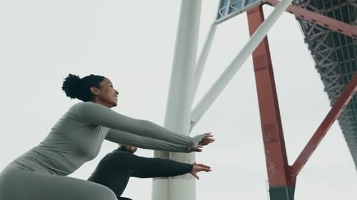 Couple Doing Squats Underneath Large Bridge