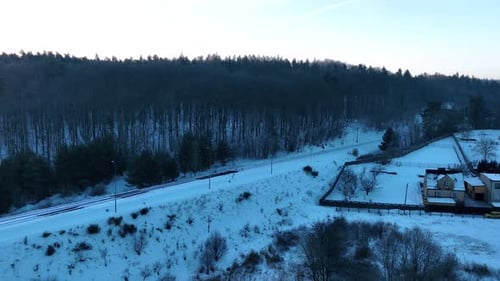 A serene winter scene featuring a snowcovered forest and a road lined trees. The landscape is