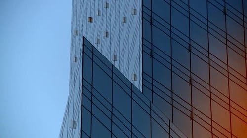 Modern architecture close up with mirrored glass walls reflecting huge orange ball of setting sun. G