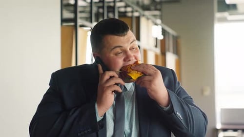 Young Adult Eats Burger While Talking on Phone