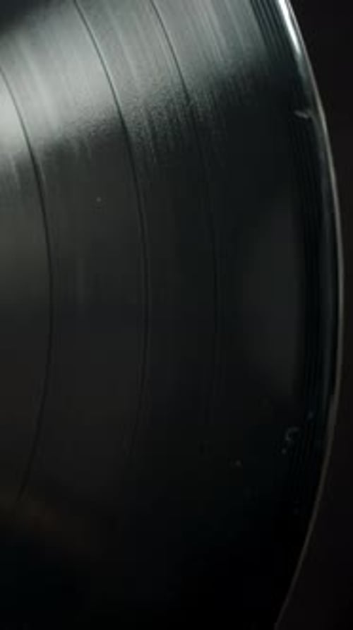 Vertical video. A black vinyl record slowly rotates, top view, close-up.