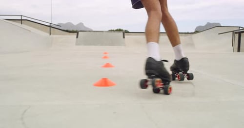 Closeup rearview of a man roller skating for hobby around cones at a skate park