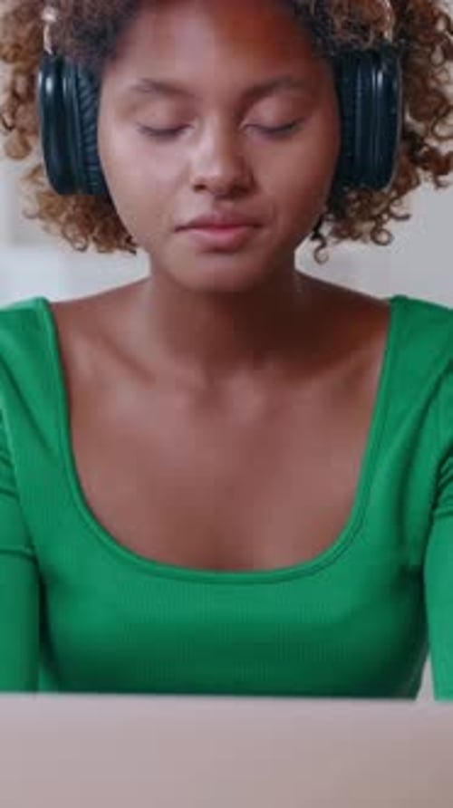 Young Woman Enjoys Music While Studying at Home in Green Top